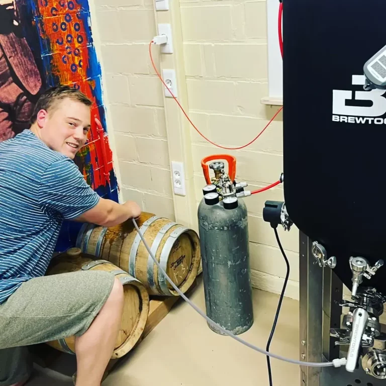 A brewer filling wooden barrels next to the brewing system
